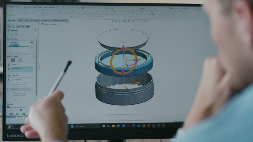 Person pointing at a computer screen showing a 3D model of a container in SOLIDWORKS software.