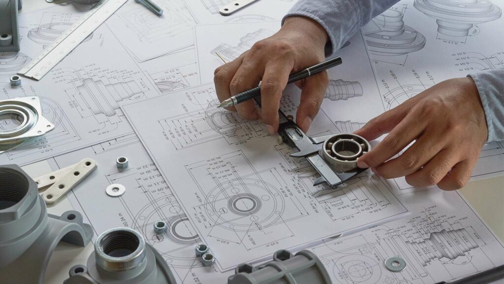 Hands measuring mechanical parts over technical engineering drawings.
