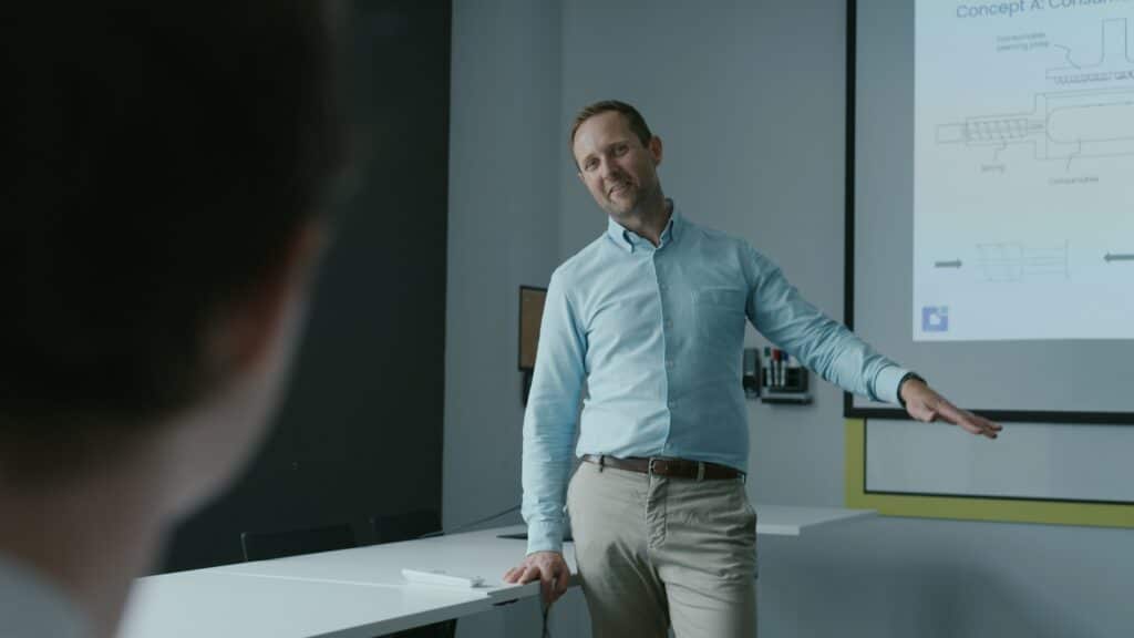 Man presenting in a conference room with a projector screen displaying diagrams.
