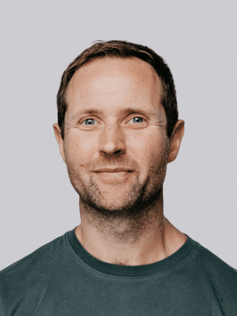 Smiling man with short brown hair and beard wearing a green shirt, against a gray background.