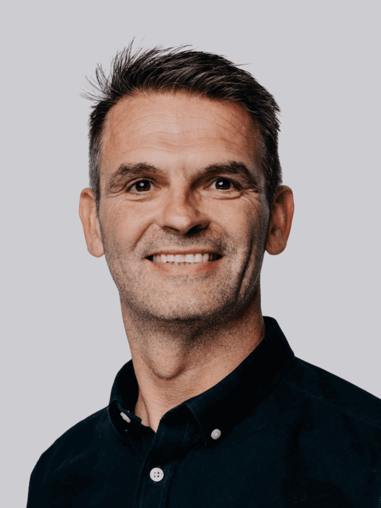 Smiling man wearing a dark button-up shirt against a plain backdrop.