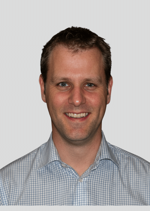 Smiling man with short hair wearing a checkered shirt against a neutral background.