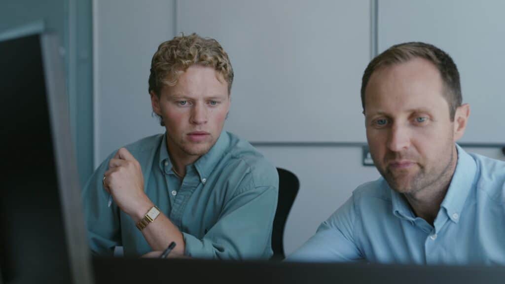 Two men focused on a computer screen in an office setting.