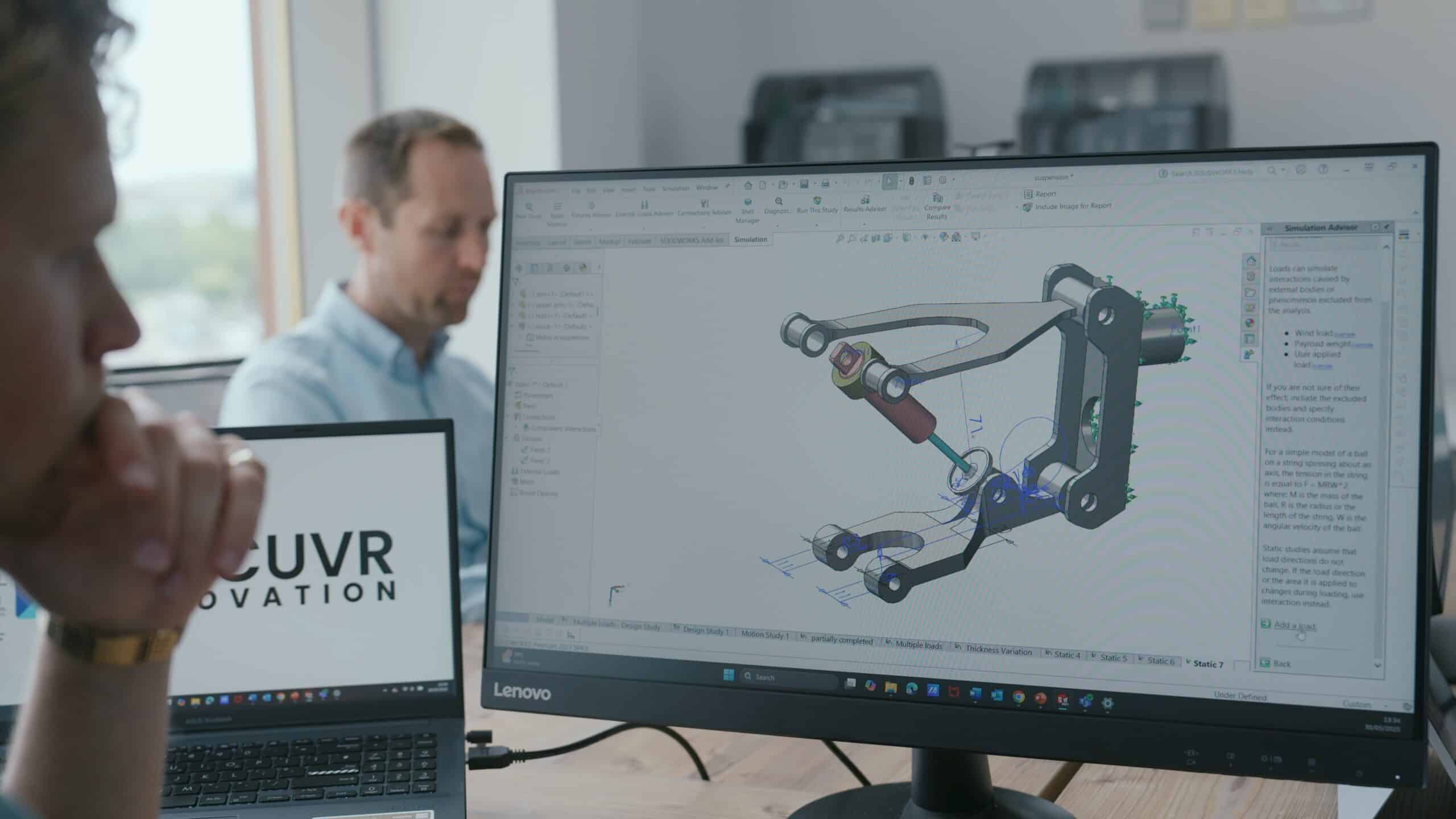 Engineer working on a CAD model on a computer screen in an office setting.