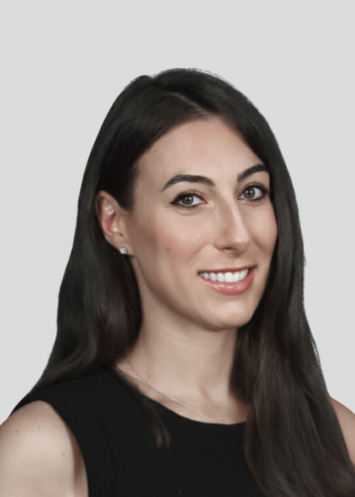 Woman with long dark hair smiling, wearing a black top against a neutral background.
