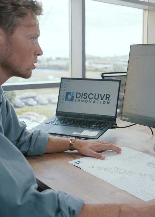 Man working at desk with DISCUVR Innovation logo on laptop screen, reviewing documents.